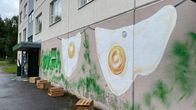 Kerrostalon seinässä on kaksi paistettua kananmunaa esittävää seinämaalausta, alapuolella puisia laatikoita.