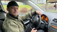 En ung man, Emil Ahlroos, sitter vid ratten i en bil. Han har på sig en grön jeansjacka och en svart stickad mössa.