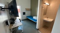 Vaalan vankilan selli. Kuva on otettu sellin ovelta selliin päin. Huoneessa on pöytätaso ja tv, taustalla näkyy punkka. 