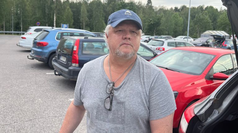 Mies seisoo parkkipaikalla pukeutuneena t-paitaan.