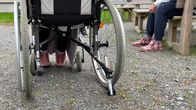 Pyörätuoli takaa kuvattuna, vieressä istuu ihminen vaaleanpunaiset Reino-tossut jalassaan.