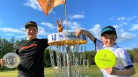 kaksi nuorta liitokiekot käsissään, nojaavat frisbeegolfkoriin