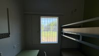 Hämärä vankilan selli, jonka ikkunasta näkyy nurmikkoa.