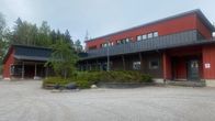 Pihan perällä on punainen rakennus. Rakennuksen edessä on viherkasvi-istutus.