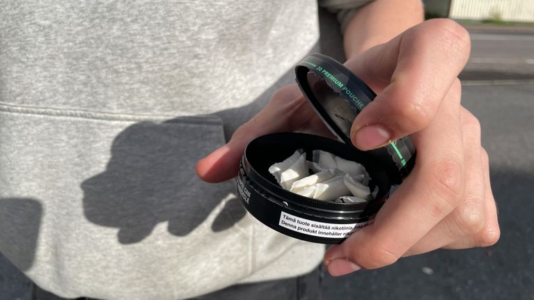 Henkilö pitelee kädessään nikotiinipussirasiaa, jonka kansi on avattu paljastaen rasian sisällä olevat nikotiinipussit.