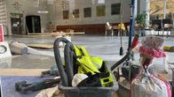 Bygggrejer samlade i en del av en större sal,  i bakgrunden stolar och soffor längs en vägg.