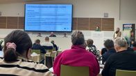 Aluevaltuuston kokous, ihmisiä istuu salissa, edessä puheenjohtaja ja kokousvirkailijoita, nuori nainen puhujanpöntössä.