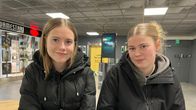 Kaksi nuorta naisoletettua istuu kauppakeskuksessa käytävällä tuoleilla. Molemmilla mustat talvitakit päällä.  