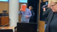 En person håller ett dokument framför sitt ansikte i rättssalen.