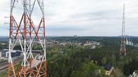 Ilmakuvan reunassa näkyy radiomasto. Taustalla siintää puita, rakennuksia sekä toinen radiomasto ja hyppytornit.