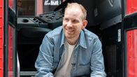 Rutger Bregman istuu punaisen bussin portailla ja hymyilee.