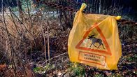 Keltainen muovipussi on ripustettu ketjuun, muovipussissa on punainen kolmio, jossa kerrotaan hirvenmetsästyksen olevan käynnissä. 