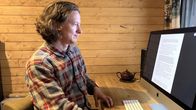 Henkilö istuu työpöydän ääressä ja katsoo tietokoneruutua, jolla on tekstiä. Taustalla puupaneeliseinä ja teekannu 18.9.2026.
