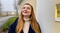 En kvinna står vid en vit pelare och tittar förbi kameran.