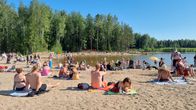 Many people on a sandy beach, with green trees and a lake in the background.
