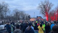 Väkijoukko kokoontunut ulkoilmatapahtumaan iltahämärässä, taustalla näkyy valaistu vanha linna ja punaiseksi valaistuja puita.