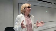 Anna-Maja Henriksson gestikulerar med händerna och talar i ett klassrum. Hon tittar åt sidan.