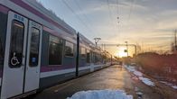Lähijuna seisoo asemalla. Edessä vähän lunta, taustalla auringonnousu.