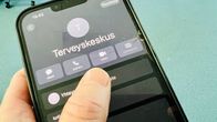Lähikuva kädestä, joka pitelee puhelinta, jonka näytöllä on teksti Terveyskeskus.