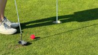 Golfari puttaa maillalla palloa kohti reikää.