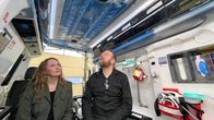 Kuvataiteilija Anne Tamminen ja muusikko Timo Seppälä istuvat ambulanssissa ja katsovat ambulanssin kattoon, jonne on teipattu sinitaivas valkoisine pilvineen.