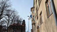 Suomenlippu liehuu kerrostalon sisäänkäynnin yläpuolella. Taustalla näkyy Lahden kaupungintalon torni.