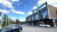 Punatiilinen  ja lasijulkisivuinen pitkä rakennus lähikuvassa. Rakennuksen eli Hotelli Tallukan vieressä on autoja rivissä parkissa. 