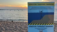 En varningsskylt för fördjupningar och kvicksand på en sandstrand i solnedgången.