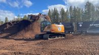 Kaivinkone siirtää suolla turvetta kuorma-autoon kirkkaassa ulkoilmassa.
