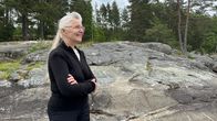 Henkilö seisoo kalliolla metsäisessä maisemassa, kädet ristissä rinnalla, taustalla havupuita.