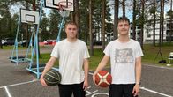 Kaksi nuorta miestä seisoo ulkokoripallokentällä, molemmilla kädessään koripallo. Taustalla on puita ja rakennuksia.