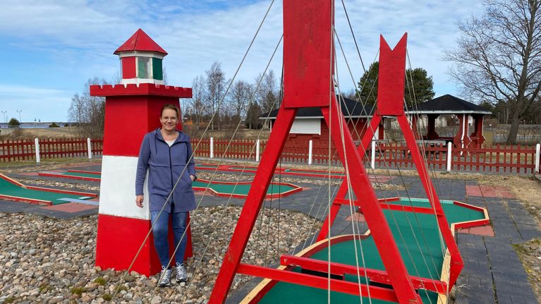 Nainen nojaa leikkipuistossa pienoismajakkaa. Ympärillä on minigolfratoja.