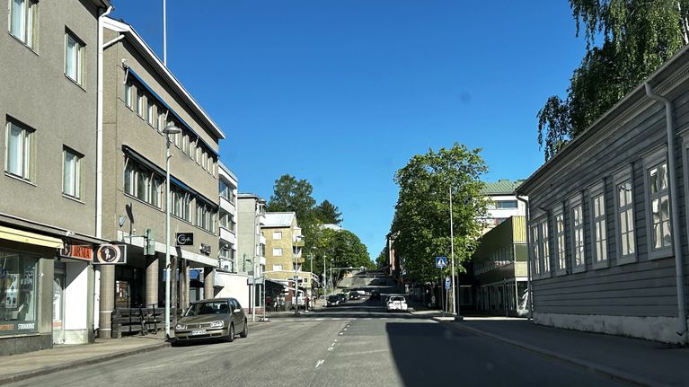 Lähikuvassa on katu, jonka varrella on rakennuksia ja pysäköityjä autoja.