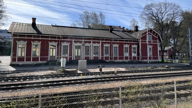 Punainen Rauman vanha rautatieasema rakennus takaalalla ja edessä vanhoja raiteita.