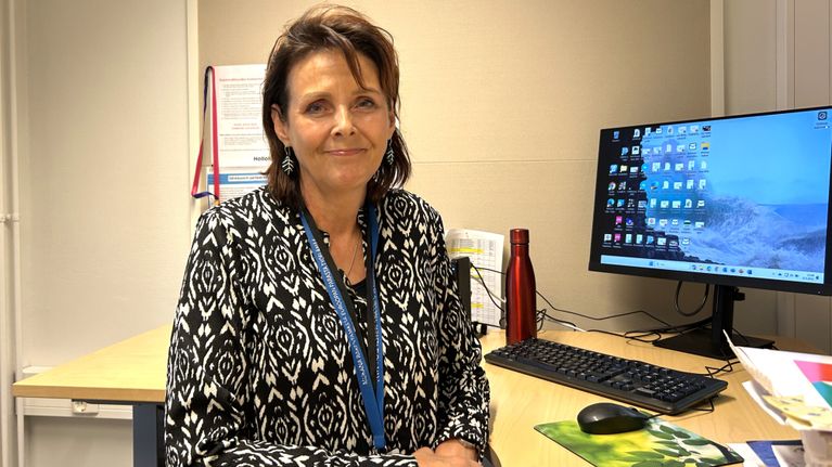 Tummatukkainen nainen istuu näyttöpäätteen vieressä ja hymyilee kameralle. Nainen on Hollolan kunnanjohtaja Päivi Rahkonen.