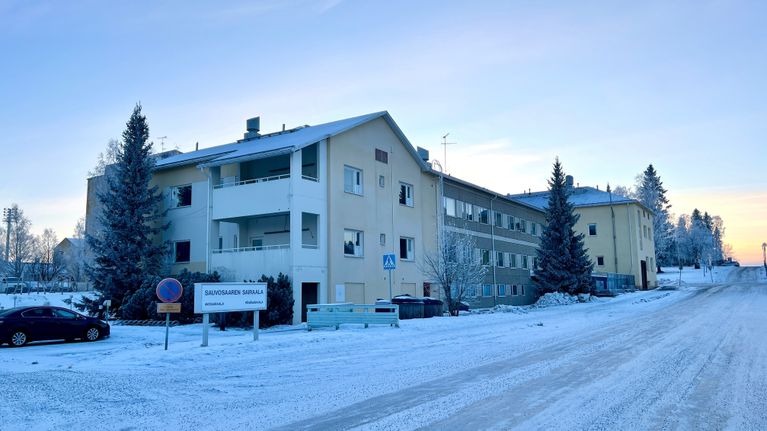 Kelta-harmaa moniosainen kerrostalorakennus lumisen tien varrella. Rakennuksen edessä kyltti Sauvosaaren sairaala.