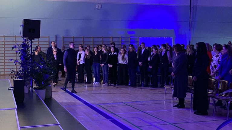Ihmiset seisovat koulun liikuntahallissa, kun presidentti Alexander Stubb saapuu.