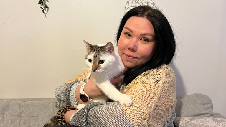 Outi Paltto istuu sohvalla kissa sylissä.