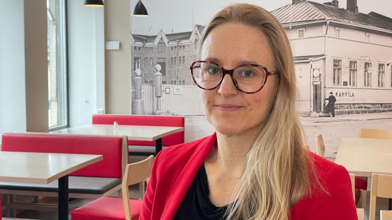 Silmälasipäinen nainen suurikokoisen valokuvaseinän edessä.