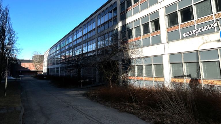 Lähikuvassa on pitkä virastorakennus, jossa on paljon ikkunoita. 