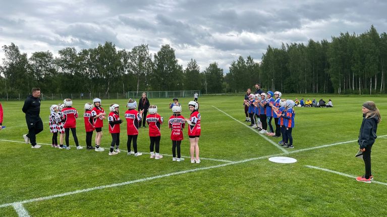 En grupp barn i sportkläder och hjälmar står uppställda i två rader på en gräsplan.