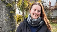 Nainen seisoo puun vieressä ja hymyilee.