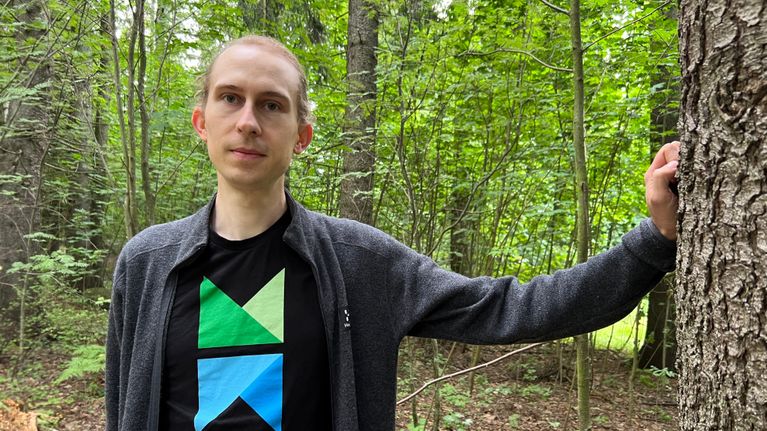 Kuvassa nuori mieshenkilö nojaa kädellään puuhun.
