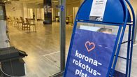 Koronarokotuspiste -teksti a-standissä, jonka takana näkyy tyhjä tila, jossa on tuoleja.