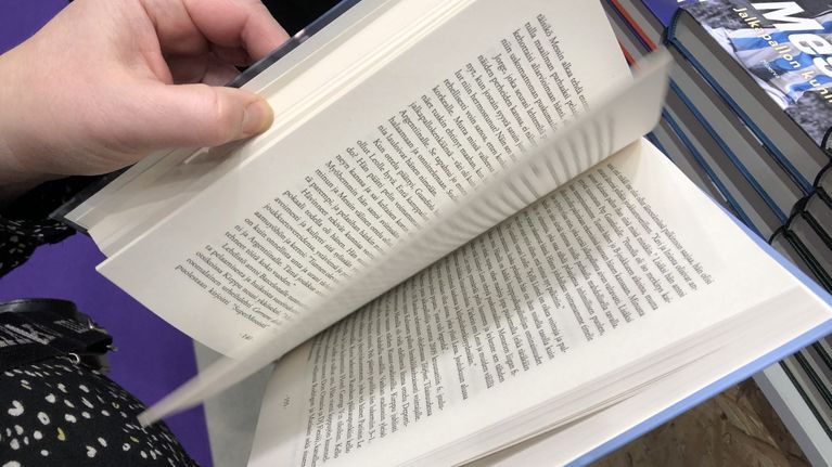 Kirja ihmisen kädessä auki niin, että lehdiltä näkyy kirjoitusta.