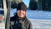 Nainen seisoo lumisessa maisemassa sukset ja sauvat kädessään.