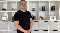 Nuori mies seisoo hyllyn edessä. Hyllyssä on eläinten tuhkille tarkoitettuja uurnia, muistoesineitä ja valokuva. 