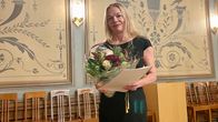 Vaaleahiuksinen nainen hymyilee kameralle kukkakimppu kädessään.