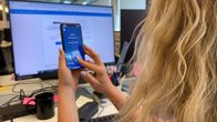Kuvassa pitkähiuksinen henkilö kirjautuu julkiseen palveluun käyttämällä puhelimen verkkopankkiaplikaation varmennepalvelua.