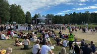 Paljon ihmisiä istuu festivaalilavan edessä nurmikolla.